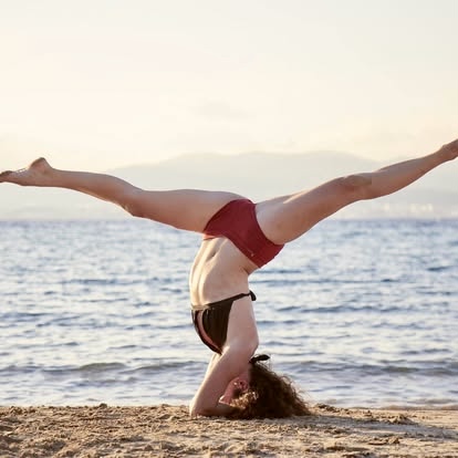 Natasha in a headstand with wide legs on the beach at sunset