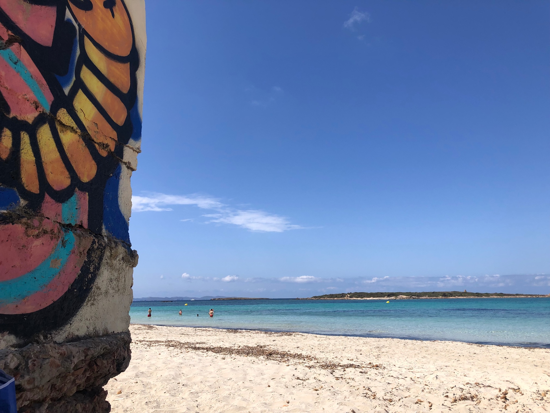 Graffiti wall beside a calm turquoise beach in Formentera