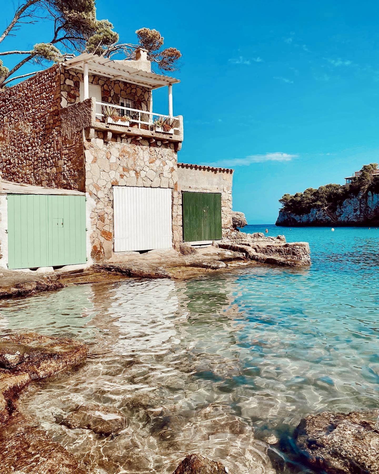 Stone boathouses with green and white doors beside a turquoise Mallorcan cove