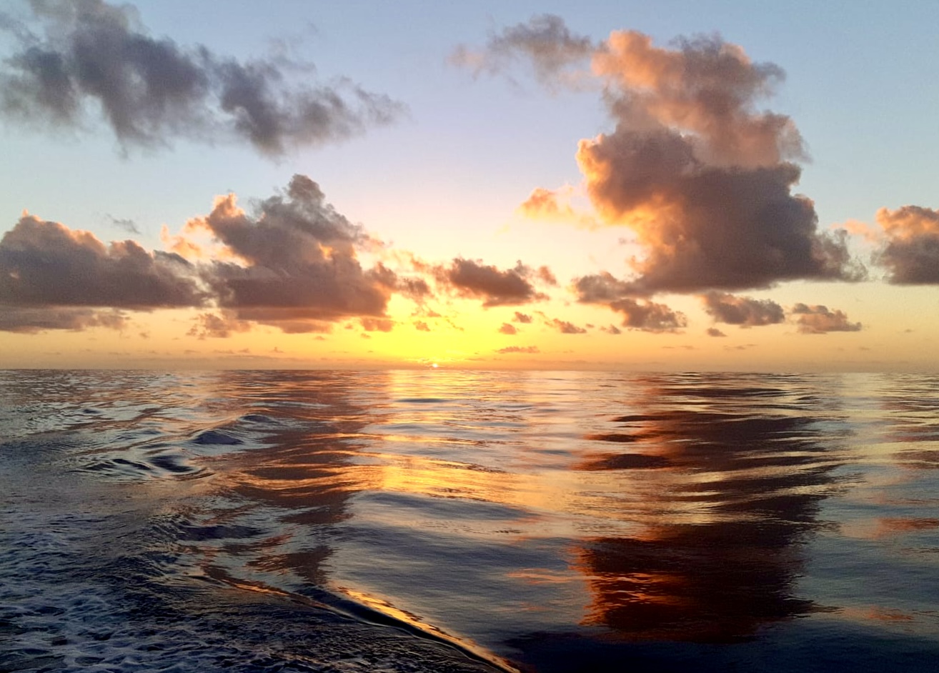 Sunset over the open ocean from the deck of a sailing boat